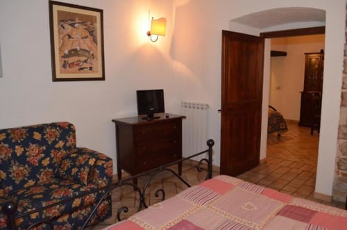 Camera da letto dell'apartment Spello B&B con divano floreale, mobili in legno, TV e pavimenti in terracotta
