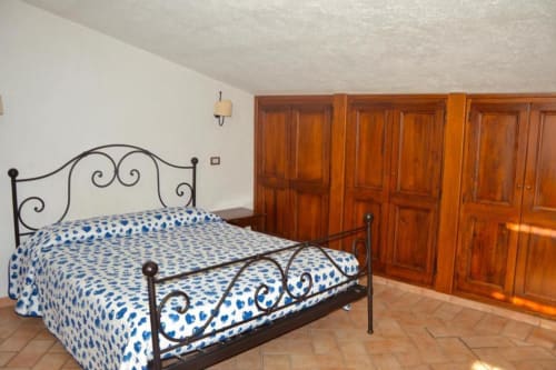 Camera da letto con letto in ferro battuto e biancheria blu decorata presso la Residenza San Jacopo a Spello, Italia, armadi in legno visibili