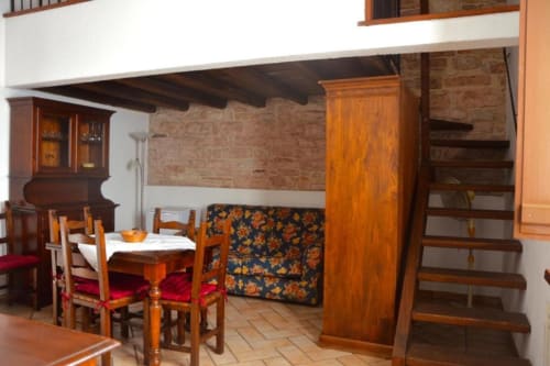 Zona living rustica della Residenza San Jacopo a Spello con tavolo in legno, divano letto e pavimenti in terracotta.