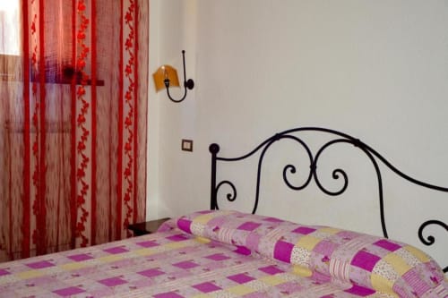 Camera accogliente alla Residenza San Jacopo a Spello con letto in ferro battuto, trapunte patchwork, tende rosse e applique