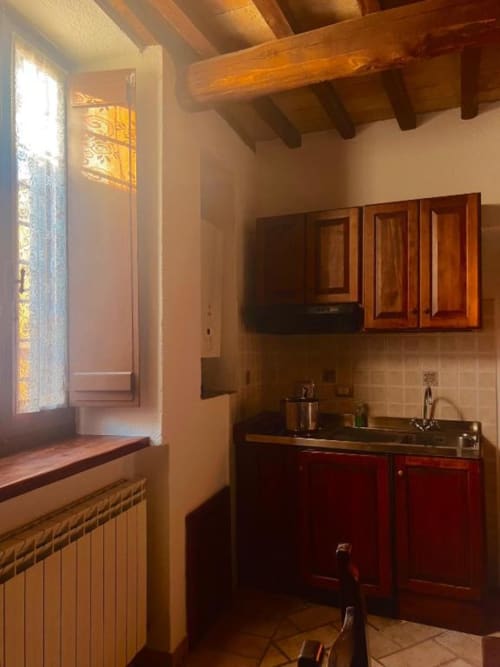 Angolo cottura rustico nell'appartamento di Spello con travi in legno, mobili rossi e ampia finestra con vista sulla città