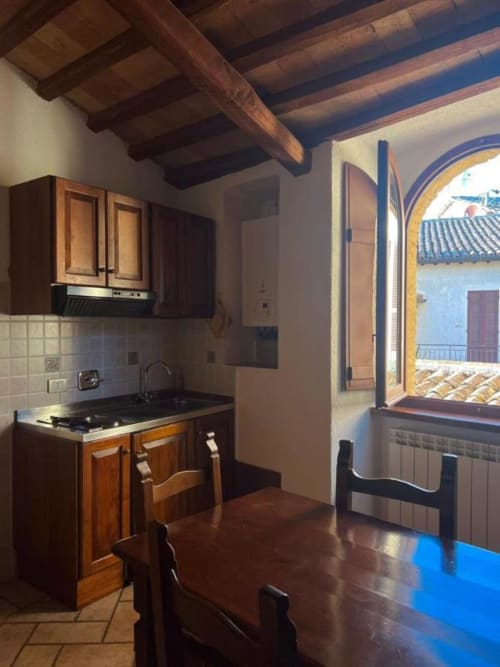 Cucina rustica con travi in legno, mobili scuri e finestra ad arco con vista su Spello, Italia presso Residenza San Jacopo B&B