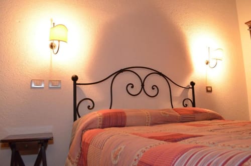 Camera da letto in Residenza San Jacopo a Spello con letto in ferro battuto ornamentale, applique calde e biancheria a righe arancioni