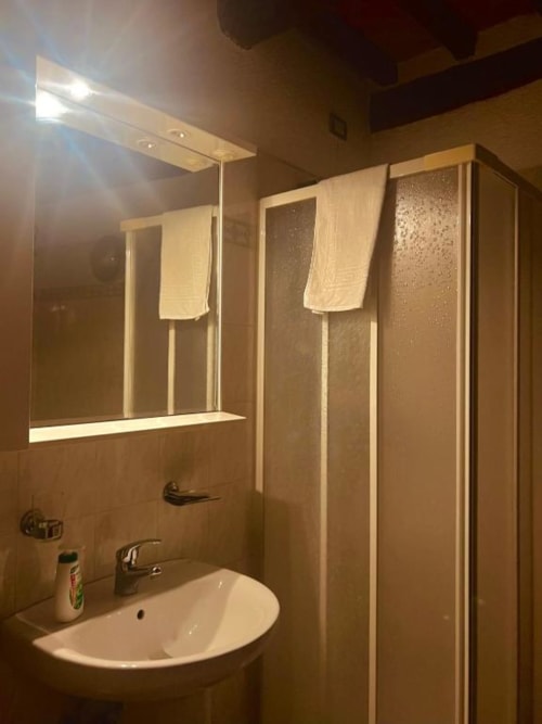 Bagno moderno nell'appartamento Residenza San Jacopo a Spello, con specchio illuminato, lavabo bianco, box doccia e asciugamani