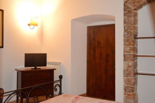 Camera da letto della Residenza San Jacopo a Spello con letto, scrivania, TV, porta in legno e illuminazione calda
