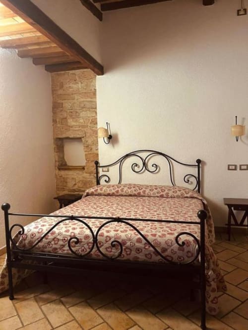 Camera da letto con letto in ferro battuto e biancheria decorata presso la Residenza San Jacopo, B&B a Spello con muri in pietra a vista