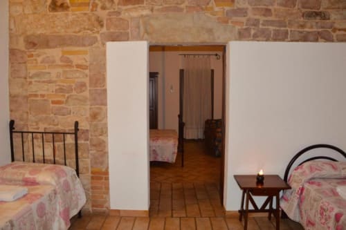Camera rustica nel B&B di Spello con letti gemelli, pareti in laterizio e pavimenti in legno che si aprono su stanze comunicanti.