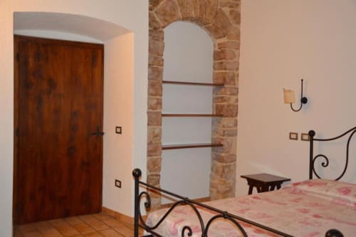 Camera rustica del B&B di Spello con letto in ferro battuto, arcata in pietra, porta in legno e pavimenti in cotto