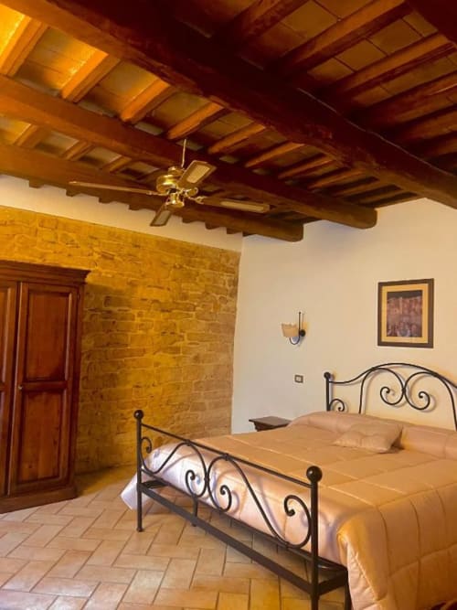 Camera rustica della Residenza San Jacopo a Spello con travi in legno a vista, letto in ferro battuto, pavimenti in cotto e pietra