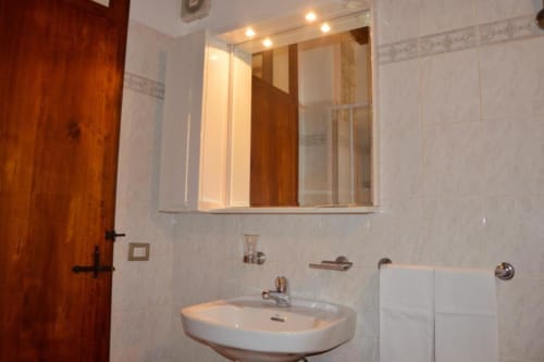 Bagno moderno della Residenza San Jacopo a Spello con pareti rivestite in piastrelle bianche, lavabo, specchio illuminato e porta in legno