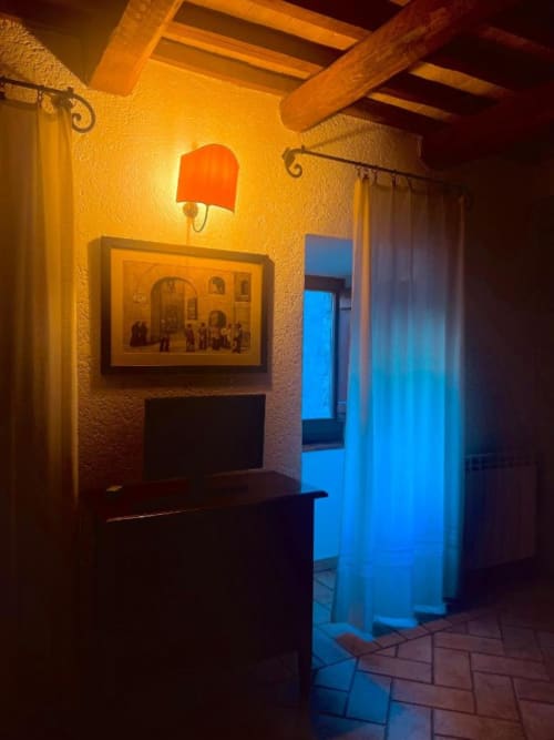 Caldo corridoio rustico alla Residenza San Jacopo a Spello con pavimenti in terracotta, travi a vista e applique luminose