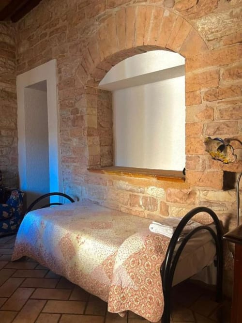 Camera accogliente in B&B a Spello con volte in laterizio a vista, letto singolo con copriletto decorato e finestra ad arco con vista sulla città