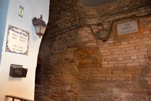 Storico corridoio in mattoni presso la Residenza San Jacopo a Spello con muri in pietra rustica, cartelli stradali italiani e lampione d'epoca
