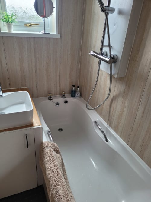 Modern bathroom at Jane's B&B Guisborough with white bathtub, rainfall shower head, wooden wall panels, and sink with