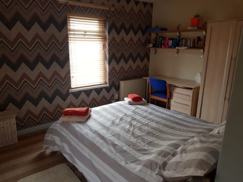 Cozy bedroom at Jane's B&B in Guisborough with chevron wallpaper, striped bedding, desk, and natural window light