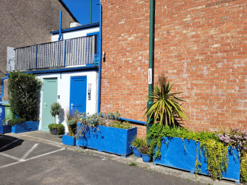 Jane's B&B apartment entrance in Guisborough with blue door, balcony, and potted plants on brick exterior