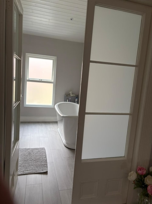 Modern bathroom at Eglinton Road Bray with freestanding tub, tiled flooring, and natural light from window