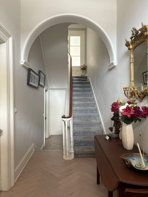 Elegant hallway at Eglinton Road Bray with arched doorway, staircase, and decorative flowers in cream vase