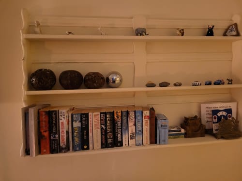 Cream shelving unit displaying books, decorative spheres, toy vehicles, and collectibles in Jane's B&B villa room in