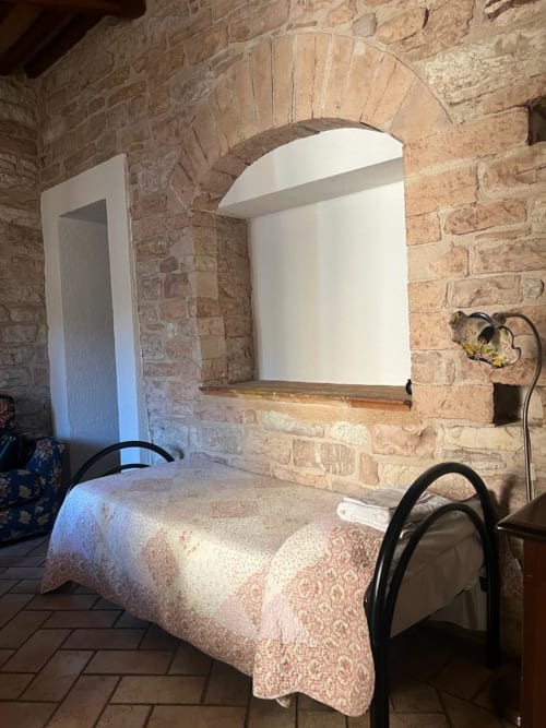 Camera con muri in laterizio, nicchia ad arco, testata bianca, copriletto decorato e sedia in metallo nero presso Residenza