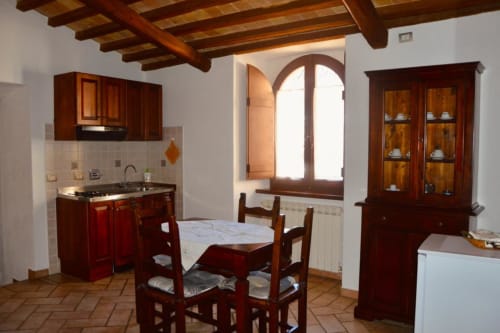 Rustica cucina e zona pranzo a Spello con travi in legno a vista, tavolo da pranzo, angolo cottura e finestra ad arco