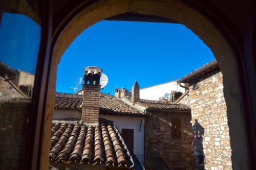 Vista attraverso l'arco di edifici con tetti in terracotta e campanile a Spello, Italia dalla residenza San Jacopo