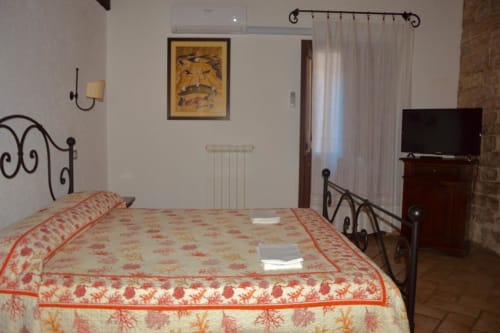 Camera da letto presso Residenza San Jacopo a Spello con letto in ferro battuto, biancheria rossa con motivi, TV e vista sulla città