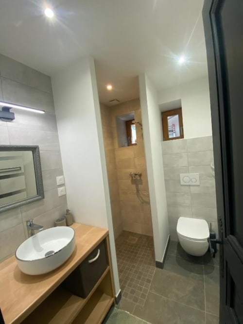 Modern bathroom at Locavilla villa in Colombes with round white sink, toilet, and walk-in shower with tiled floors.