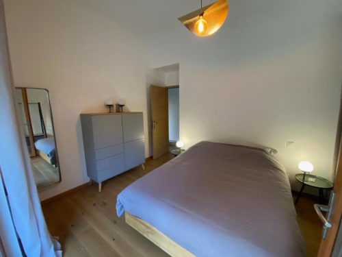 Modern villa bedroom at Locavilla in Colombes with queen bed, blue dresser, mirror, pendant light, and wooden flooring