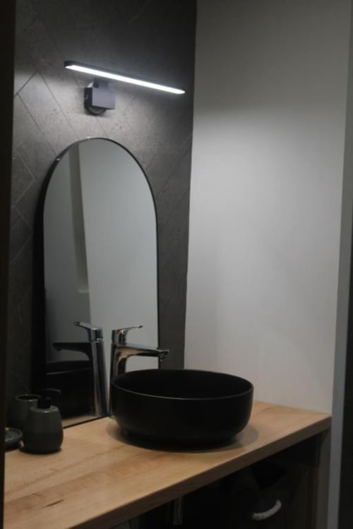 Modern bathroom sink with black vessel bowl and oval mirror at Locavilla villa, Colombes, with LED lighting above.