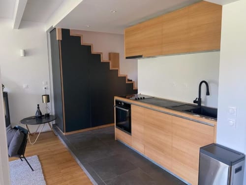 Modern kitchen in Locavilla villa with wooden cabinetry, black countertops, stainless steel appliances, and staircase access