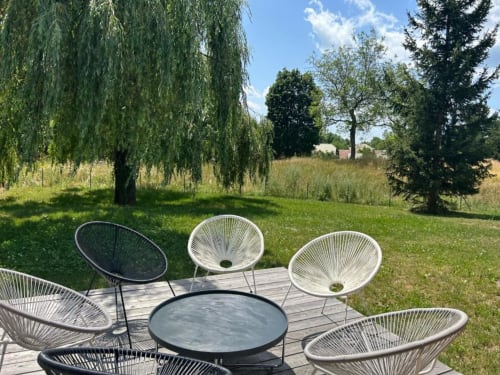 Modern outdoor seating area at Locavilla villa in Colombes with woven chairs around a round table, overlooking lush green