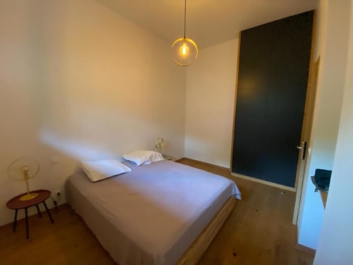 Modern bedroom at Locavilla villa in Colombes with bed, pendant light, wooden floor, and dark door