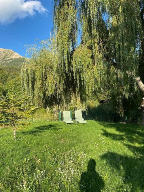 Two lounge chairs on lawn beneath weeping willow trees with mountain views at Locavilla villa in Colombes