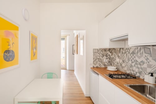 Cucina moderna nell'appartamento Art House Rome con banconi in legno, armadi bianchi, piastrelle decorate e opera d'arte gialla