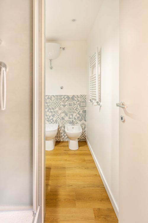 Bagno moderno in appartamento Art House Roma con piastrelle decorate, wc, bidet, pavimento in legno e sanitari bianchi