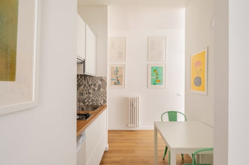 Appartamento Art Gallery moderno a Roma con cucina bianca, tavolo in legno, sedie verdi e opere d'arte colorate alle pareti