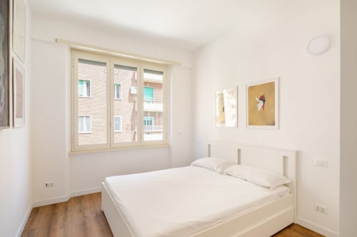 Camera da letto minimalista luminosa all'Art House Roma con letto matrimoniale, pavimenti in legno, finestra con vista sulla città e moderna opera d'arte