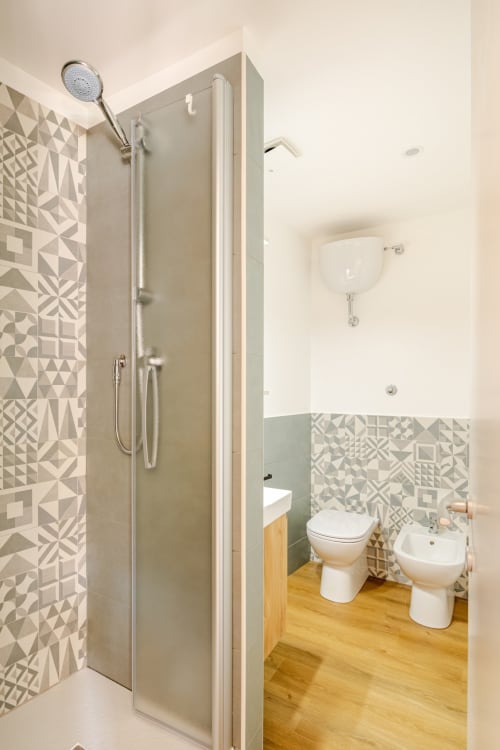 Bagno moderno con piastrelle geometriche, doccia walk-in, toilet, bidet e pavimento in legno nell'Art House apartment