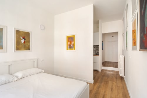 Camera da letto moderna con letto bianco, parete divisoria minimalista, pavimenti in legno e opere d'arte colorate alle pareti