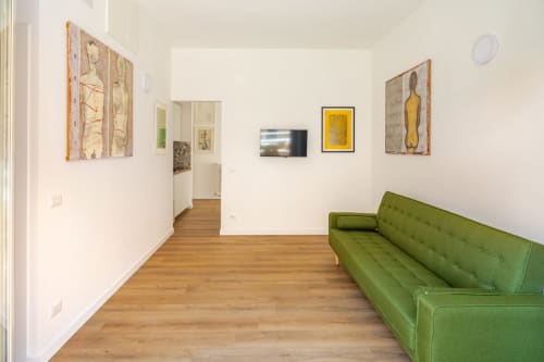 Spazio galleria in moderno appartamento a Roma con divano verde, pavimenti in legno e opere d'arte contemporanea su pareti bianche