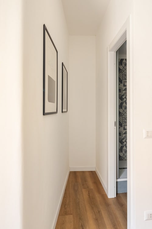 Corridoio minimalista moderno in appartamento Art House Roma con pavimentazione in legno e opere d'arte incorniciate su pareti bianche