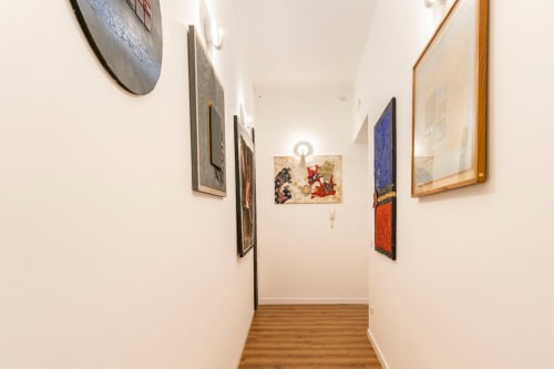 Stretto corridoio in Art House Roma con quadri incorniciati su pareti bianche e pavimento in legno