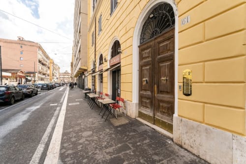Facciata gialla dell'Art House apartment a Roma, con porte in legno, tavolini all'aperto e auto parcheggiate sul selciato