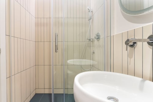 Moderno bagno di Art House Roma con lavabo d'appoggio, box doccia in vetro e rivestimento piastrellato verticale
