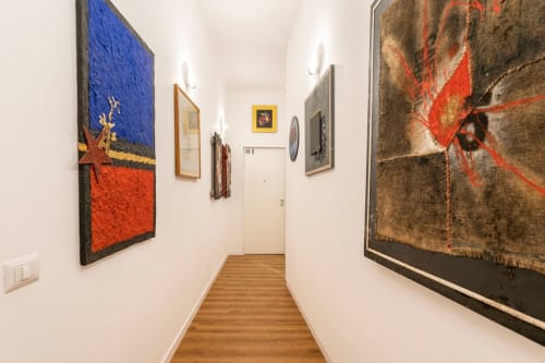 Stretto corridoio in un appartamento artistico romano con dipinti contemporanei in stile astratto con tonalità di blu, rosso e oro su parete bianca