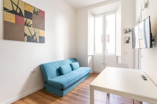 Soggiorno moderno dell'Art House hotel a Roma con divano blu, scrivania bianca, opere d'arte, TV e porte in vetro