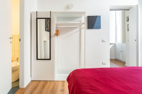 Camera da letto luminosa e moderna con letto a baldacchino rosso, pavimenti in legno e bagno privato nell'appartamento Art House Roma
