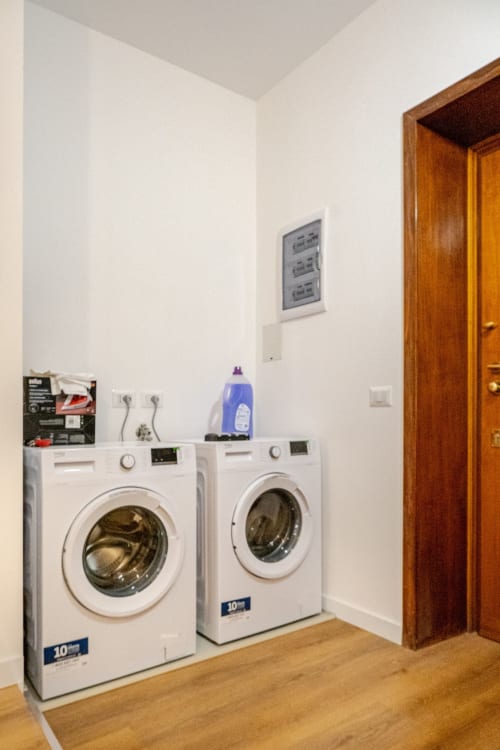 Lavanderia con due lavatrici bianche, detersivi e porta in legno nell'Art House a Roma