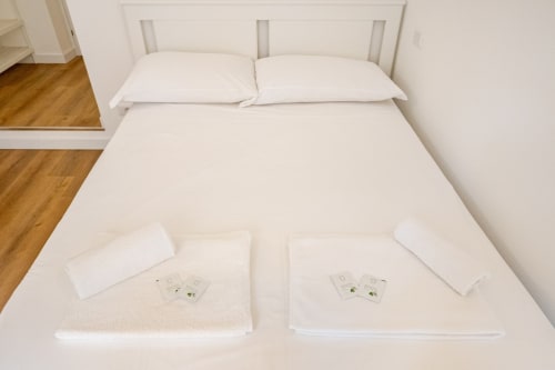 Due letti bianchi con cuscini e asciugamani all'Art House di Roma, pavimento in legno visibile
